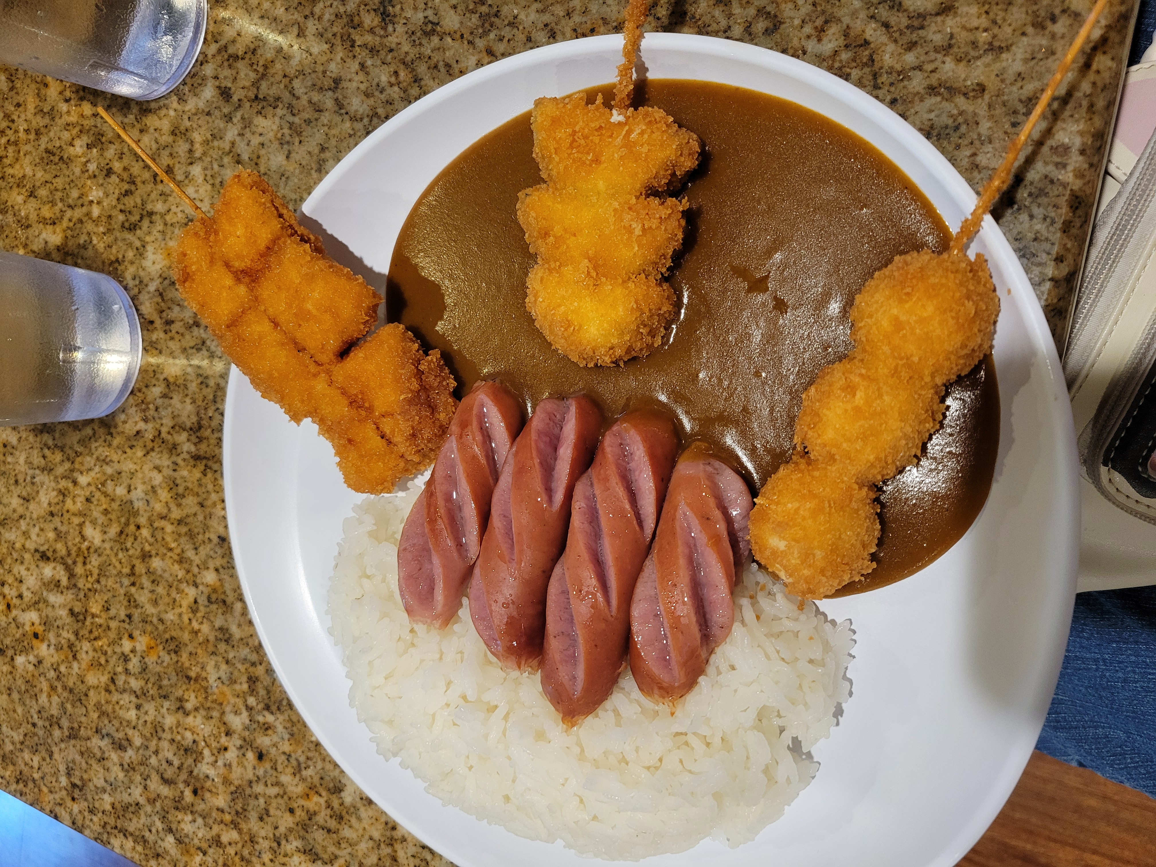 Plate of curry with three kurobuta sausage, chicken, zucchini, and quail egg kushi.